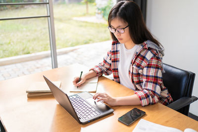 Young woman using mobile phone while sitting on table