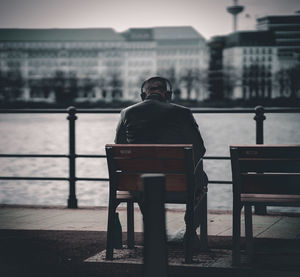 Rear view of man sitting on bench in city