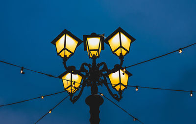 Close-up of illuminated street  lantern against blue sky