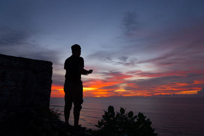 Silhouette man standing by sea against sky during sunset