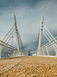 Rear view of woman walking on bridge against cloudy sky