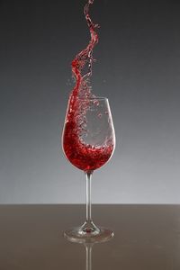 Red wine splashing in glass on table against gray background