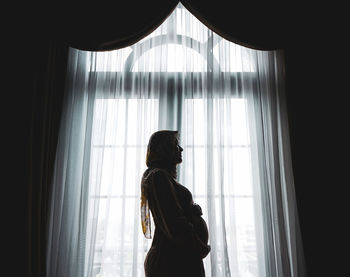 Side view of woman looking through window at home