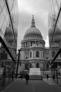 People walking in front of building against sky in city