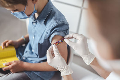 Nurse putting adhesive bandage on boy's arm at vaccination center