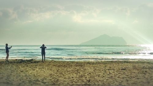 People enjoying at beach against cloudy sky on sunny day