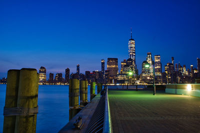 Illuminated buildings in city against clear blue sky