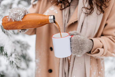 A girl pours hot tea outside in winter from a thermos into a white mug