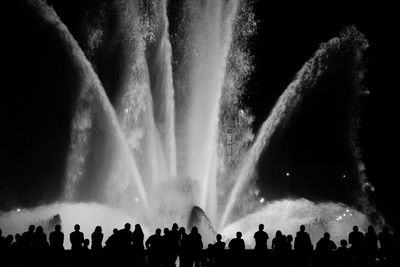 Silhouette crowd standing against illuminated fountain at night