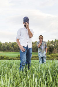 Farm worker covering face with hats while standing on farm against sky during sunset