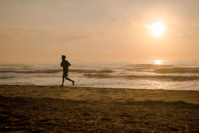 Silhouette man run on beach with sunrise and sea background