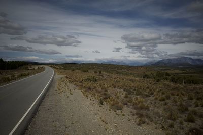 Empty road amidst field against sky