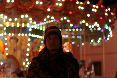 Young woman standing below illuminated christmas lights at night