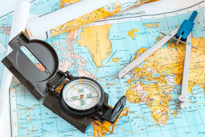 High angle view of navigational compass and drawing compass on world map