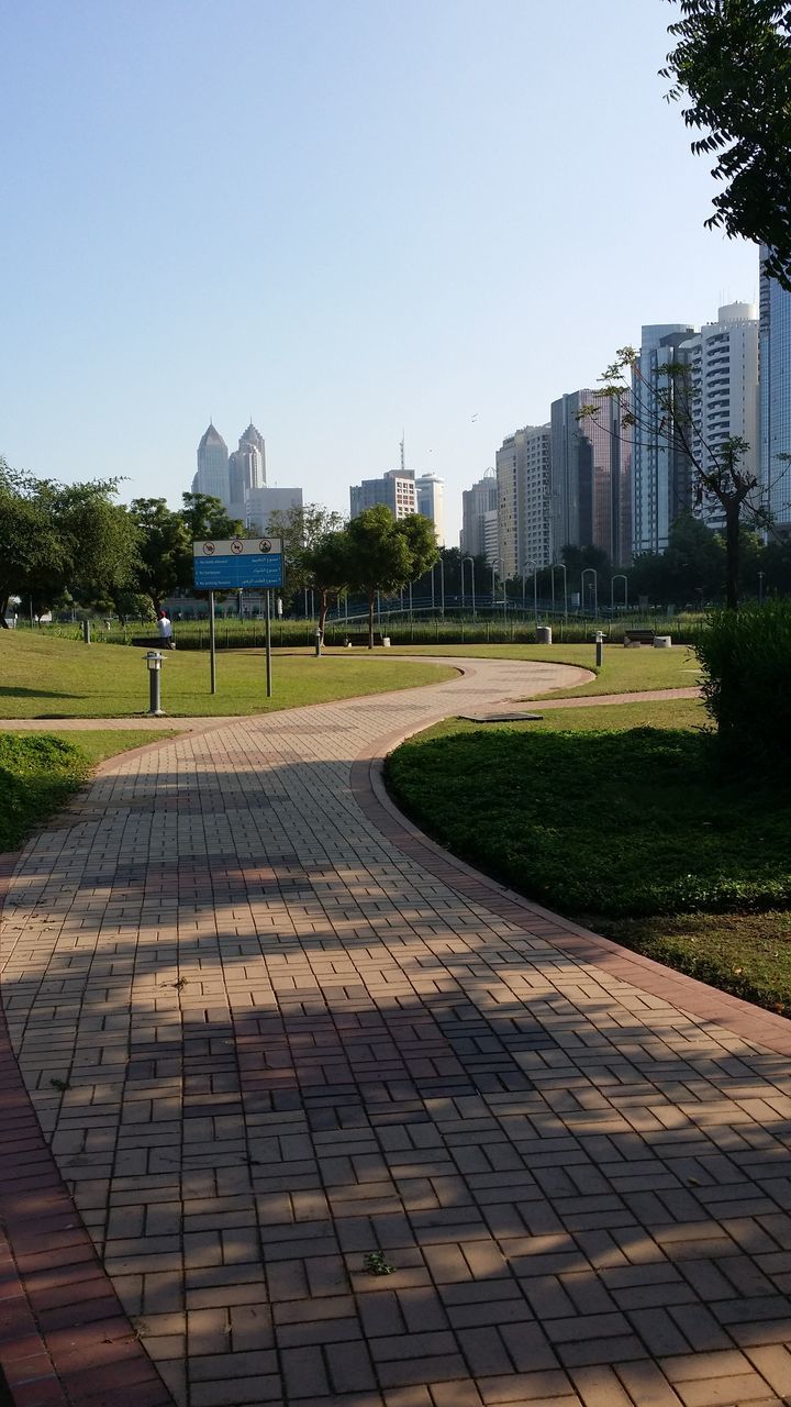 architecture, building exterior, built structure, tree, city, clear sky, building, city life, day, street, outdoors, sunlight, residential structure, transportation, residential building, growth, sky, incidental people, road, in a row