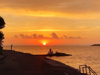 Silhouette people on sea against sky during sunset