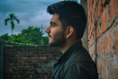 Close-up of young man standing against brick wall