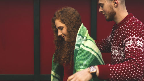 Beautiful young guy and girl cuddling in a green plaid and christmas colors on a red background.