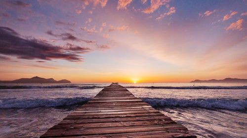 Wooden jetty over sea against cloudy sky during sunrise