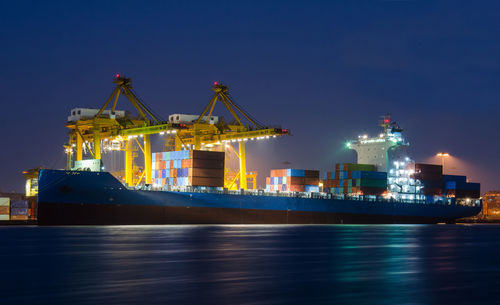 Illuminated commercial dock by sea against sky at night