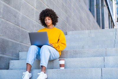 Young woman using mobile phone while sitting on staircase