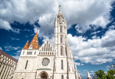 Low angle view of matthias church against cloudy sky during sunny day