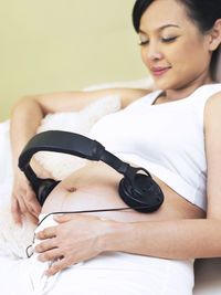 Pregnant woman wearing headphones on belly at home