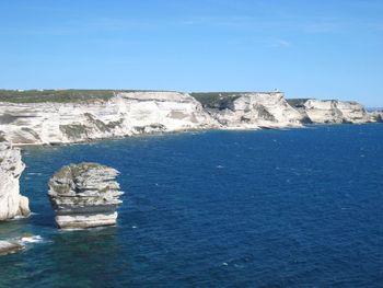 Rock formations in sea against clear blue sky