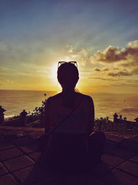 Silhouette woman sitting on beach against sky during sunset