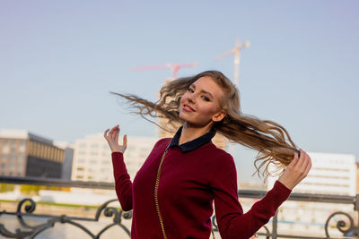 Smiling young woman standing against sky in city
