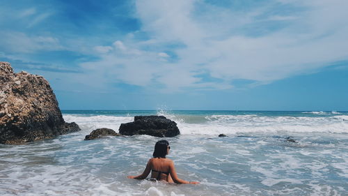 Rear view of woman in bikini at beach against sky