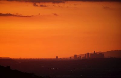 Scenic view of silhouette city against orange sky