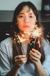 Portrait of young woman holding illuminated sparklers at home