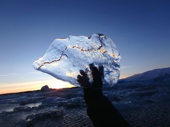 Person on rock in sea against clear sky during sunset