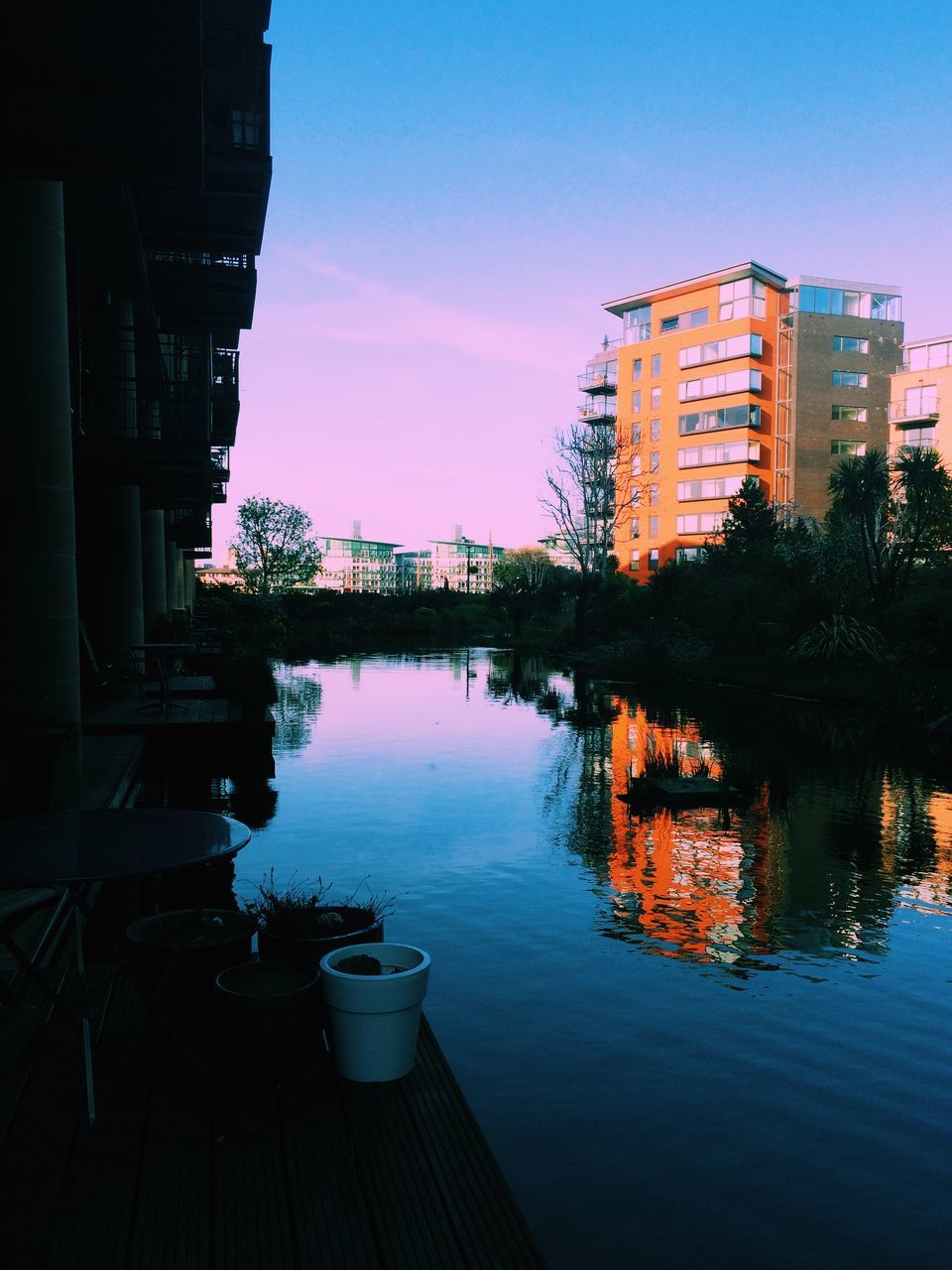 architecture, building exterior, built structure, reflection, water, sunset, sky, city, tree, residential building, residential structure, building, river, house, orange color, waterfront, illuminated, lake, dusk, no people