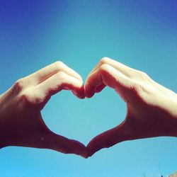 Low angle view of cropped hand against clear blue sky