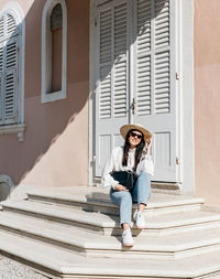 Full length portrait of young woman sitting on building