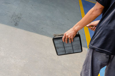 Midsection of man holding metallic equipment while standing on road