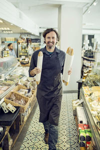 Portrait of mature male baker with loaves of bread walking in supermarket