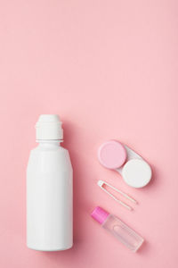 Contact lens accessories solution, container, tweezers. pink background, copy space.