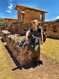 Woman siting on old ruin wall against blue sky