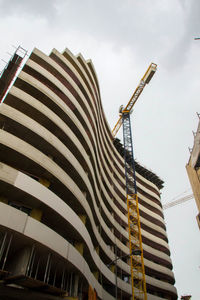 Low angle view of crane by building against sky