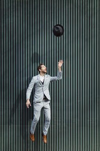 Businessman jumping while throwing hat against wall