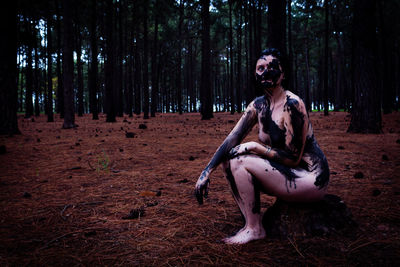 Naked woman covered with paint while sitting in forest