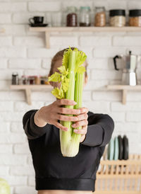 Close-up of young woman holding celery in kitchen