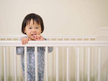 Portrait of smiling baby girl standing in crib at home