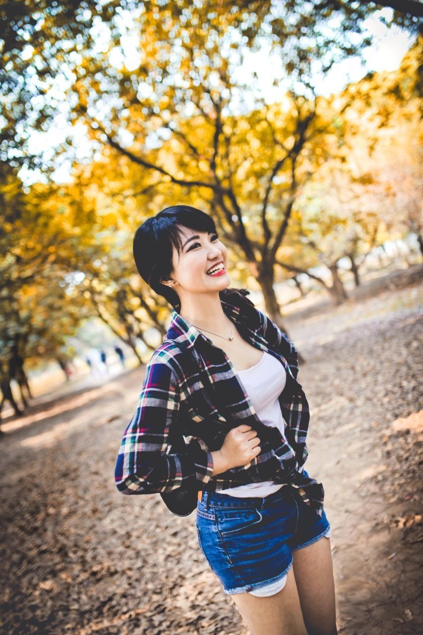 lifestyles, leisure activity, tree, casual clothing, person, young adult, young women, focus on foreground, long hair, front view, standing, looking at camera, portrait, three quarter length, park - man made space, outdoors, day