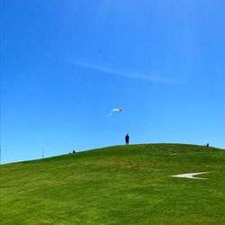 Mid distance view of man flying kite on hill against clear blue sky