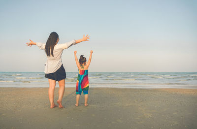 Rear view of woman with daughter enjoying at beach