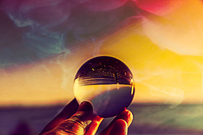 Digital composite image of hand holding glass against sky during sunset